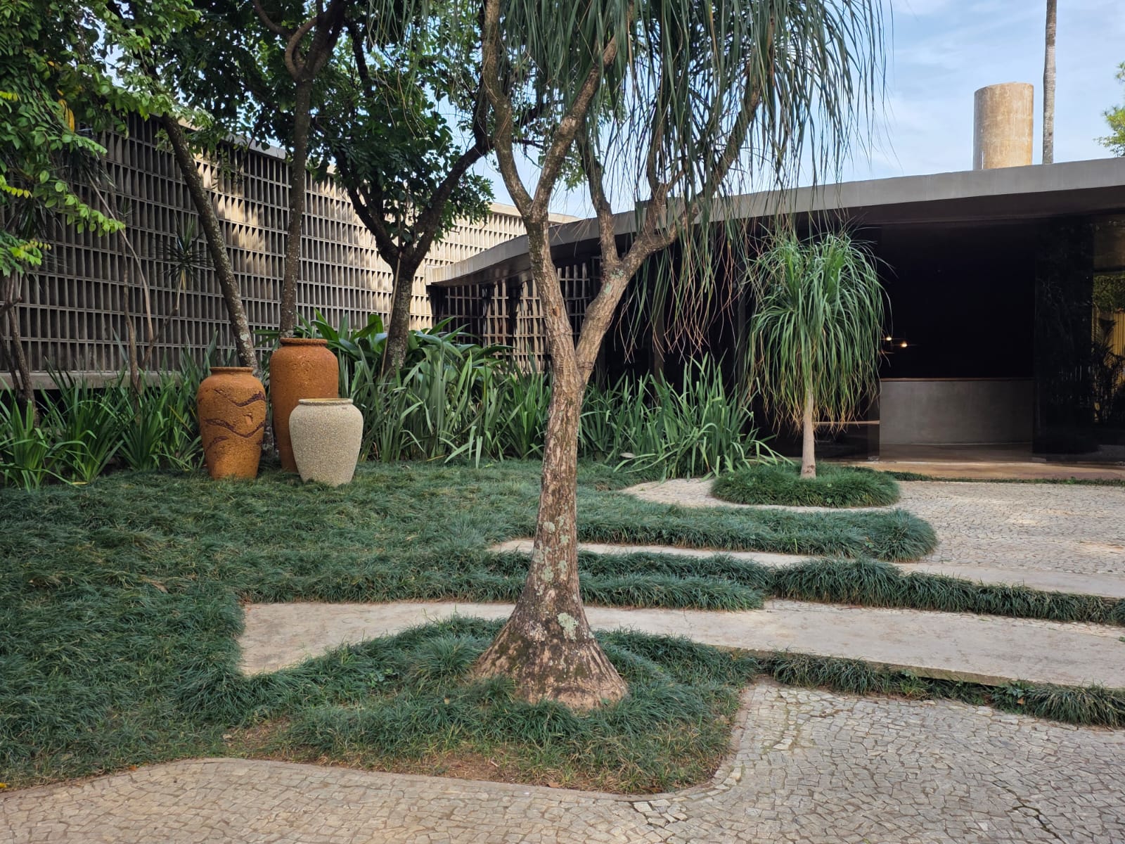 Jardim lateral com cobogós, vasos de cerâmica e vegetação tropical